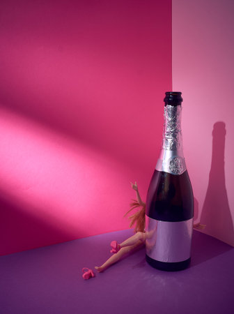 Spotlight. A bottle of sparkling wine. Behind the bottle is a doll with raised arms and legs and...