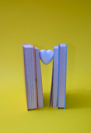 Books in an upright position, between the books a little white heart, on a yellow background. Text space. Book lovers, reading is in, concept. Minimal style.の写真素材