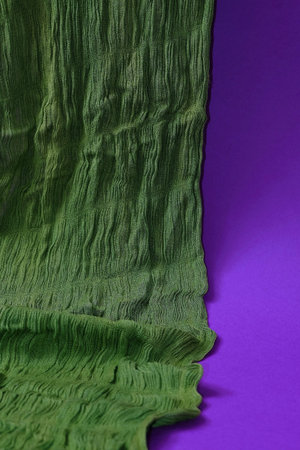 Green scarf on a purple background. Text space. Fashion, design, decoration, arranging concept....