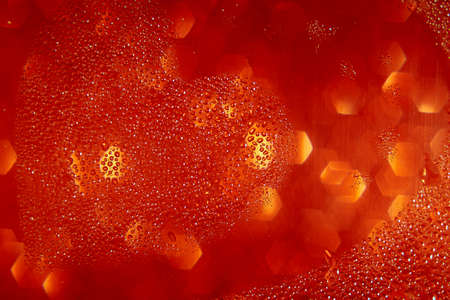 On a blurred red glittering background, drops of water in the shape of a heart.の写真素材