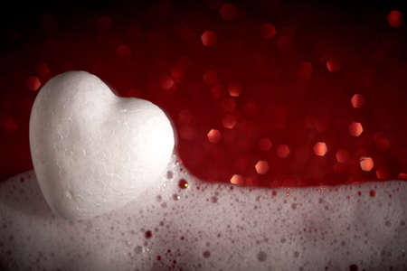 Soap foam, white heart on a blurred shimmering red background. Closeup.の写真素材