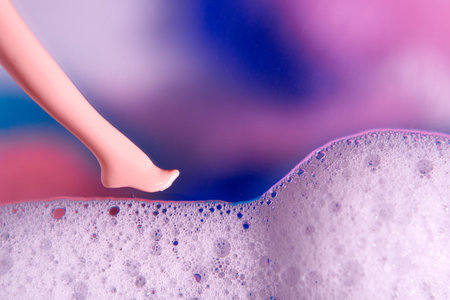 White foam, doll's foot on a blurred multicolored background.