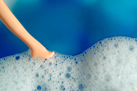 Blue blurred background, white bubble foam and doll's leg.の写真素材