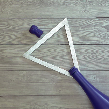 Purple bottle of champagne and a silver triangular frame on a bright gray wooden background....