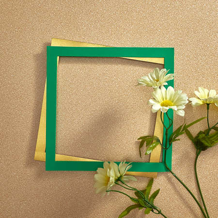 White flowers, green and gold frame on a light sandy background. Text space. Top view. Minimal style. Spring, daisy, holidays.の写真素材