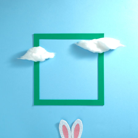 Fluffy clouds, green frame and bunnies white pink ears on a pastel blue background. Text space. Top view. Minimal style.の写真素材