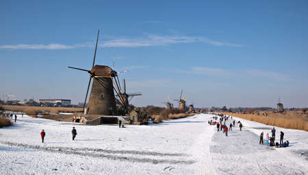 People having fun and ice skating on a frozen canal along windmills at the Unesco World Heritage Site Kinderdijk in the Netherlands in winter.のeditorial素材