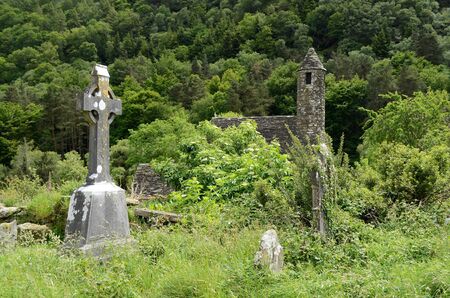 A celtic cross on the overgrown graveyard next to the medieval church of St. Kevin at the monastic heritage site Glendalough, south of Dublin in Ireland.の写真素材