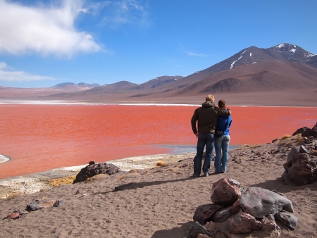 Young tourist couple admiring the Red Lagoon, or Laguna Colorada, on the Altiplano near Uyuni inside Eduardo Avaroa National Reserve in Bolivia at 4300 m above sea level.  The red color of the water is caused by sediments and algae. The white part is boraの写真素材
