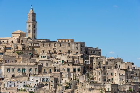 Old houses and a church in ancient architecture in the same kind of stone in a town built upon a hill, known as the Sassi di Matera in Basilicata, Italy.の写真素材