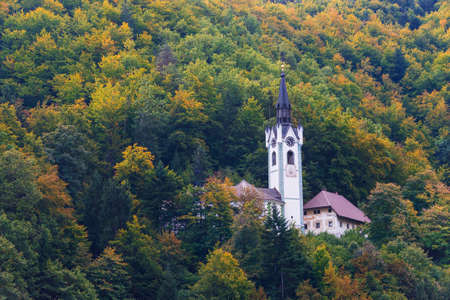 A roman catholic church in a forest on a hill surrounded by trees with autumn foliage in fall season near Bled in Slovenia.のeditorial素材
