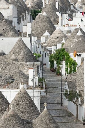Empty street lined by typical traditional white plaster trulli houses with cone-shaped roofs in the early morning in the southern Italian city Alberobello in Apulia, Italy.の写真素材
