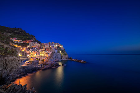 The pretty colorful town of Manarola, with lights on it, built on a cliff above the Mediterranean...