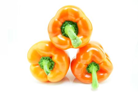 three fresh orange paprika stacked in a pile  Capsicum Annuum  on a white backgroundの写真素材