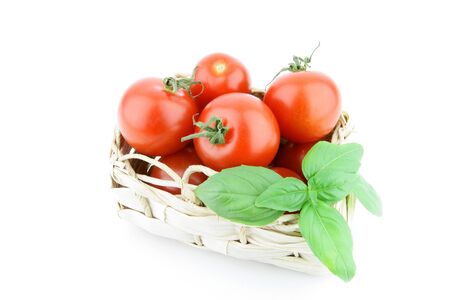 Fresh ripe tomatoes in a woven basket on a white background の写真素材
