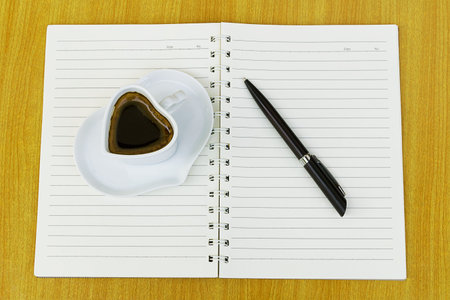 Office table with Notebook, Pen and black coffee cup. View from above with copy space