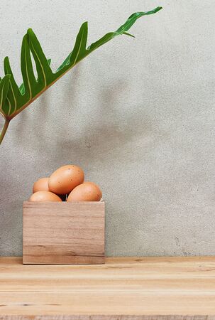 Eggs in a wooden box on a wooden table under a foliage plant.の写真素材