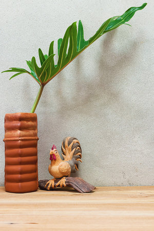 foliage plant in vase and chicken statue made of sawdust on a wooden table.