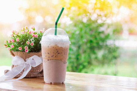 Ice coffee in plastic cups on the wooden desk with background natural blur bokeh and ray of light orange. Has copy spaceの写真素材