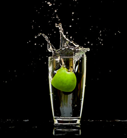 Apple green in water splash out of glass on black background. with light and shadow.の写真素材