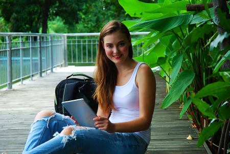 Beautiful woman sitting and searching website on smartphone in the public parkの写真素材