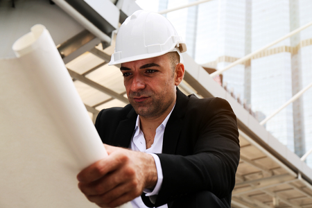 Close-up engineering man looking structure plan on paper at outdoor and building background.の写真素材