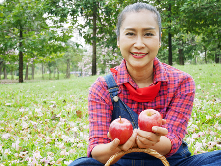 Beautiful senior woman holding red apple at public park.の写真素材