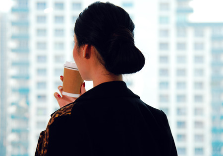 Beautiful business woman eating coffee before start working and office building background in the city.の写真素材