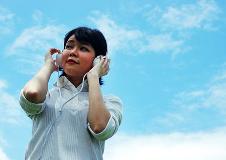 Beautiful girl teen holding headphone and listening music, Blue sky background.の写真素材