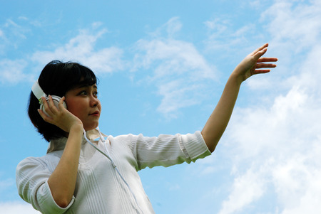 Beautiful girl teen holding headphone and listening music, Blue sky background.の写真素材