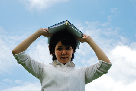 Beautiful girl teen holding book on head, Blue sky background.の写真素材