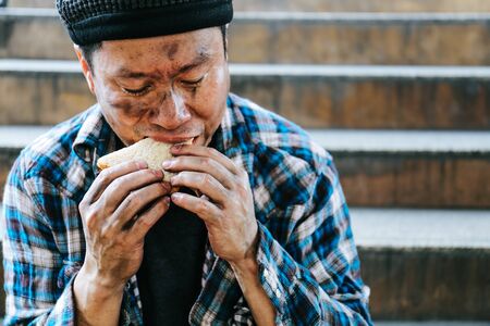 Close-up homeless man portrait eating bread on walking street.の写真素材