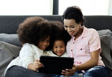 Beautiful american kid girl and mom smile portrait looking smart phone for learning at home.の写真素材