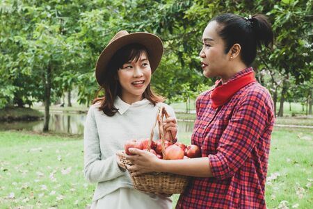 Beautiful mother and daughter are walking and eating apples in summer at garden park.の写真素材