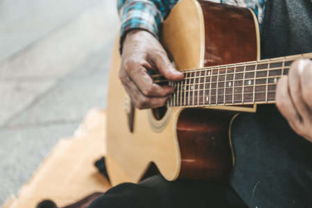 Senior homeless man sitting and playing acoustic guitar.の写真素材