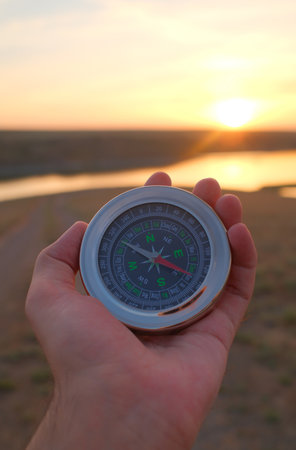 Hand holding compass during sunset over river landscape representing navigation and exploration conceptsの写真素材