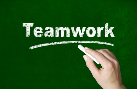 Person writing a Teamwork word with chalk on a classroom style blackboardの写真素材