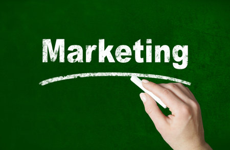 Person writing a Marketing word with chalk on a classroom style blackboardの写真素材