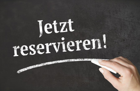 "Reserve now!" german word written in chalk on a blackboardの写真素材