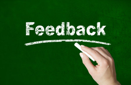 Person writing a Feedback word with chalk on a classroom style blackboardの写真素材