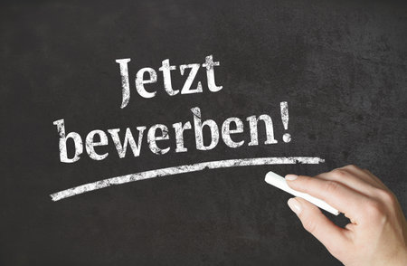 "Apply now!" german word written in chalk on a blackboardの写真素材