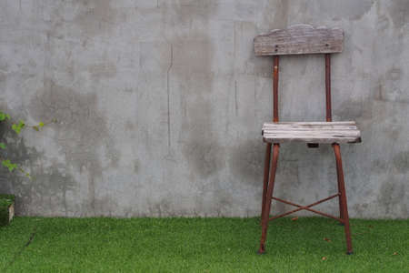 An old wooden-steel chair is put on field in front of concrete wallの写真素材