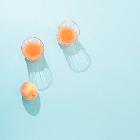 Top view of glasses with juice and peach on blue background. Minimal flat lay.の写真素材