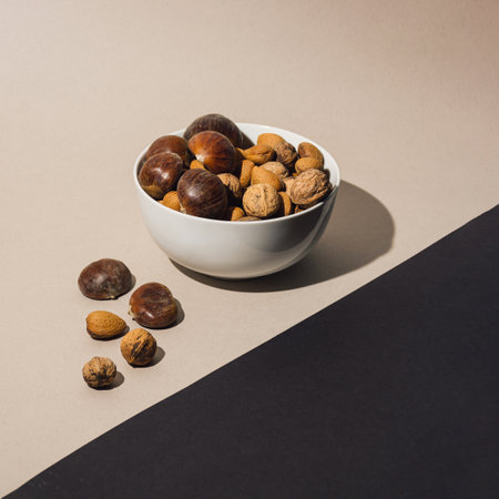 Bowl filled with almonds, chestnuts and walnuts placed on black and cream backgorund. Autumn fruit concept.の写真素材