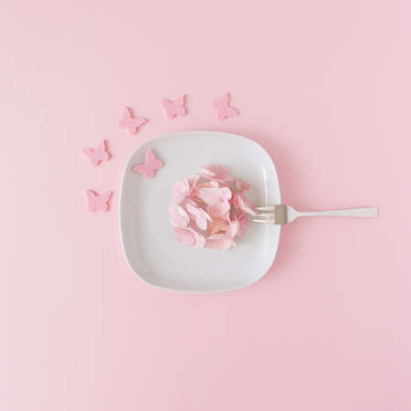 Creative composition made of pink flowers arranged on a plate with butterflies and fork.Fun romantic concept. Flat lay.の写真素材