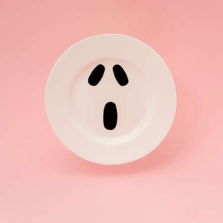 Scary face on a white plate floating against light pink background. Minimalist Halloween concept.の写真素材