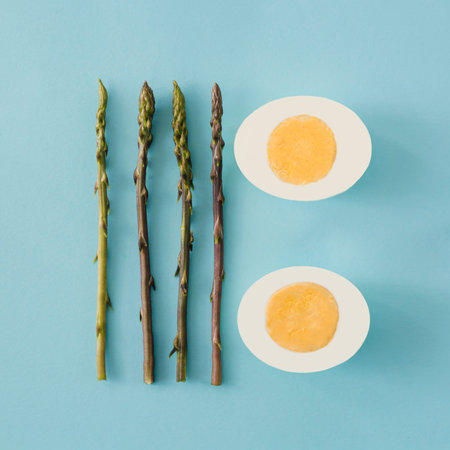 Wild asparagus and hard boiled egg arranged on light blue background. Seasonal healthy food minimal...