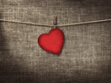 Valentine card heart shaped from old red paperr hanging on a clothesline on a linen backgroundの写真素材