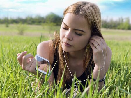 young blond woman listening to music with headphones outdoorsの写真素材