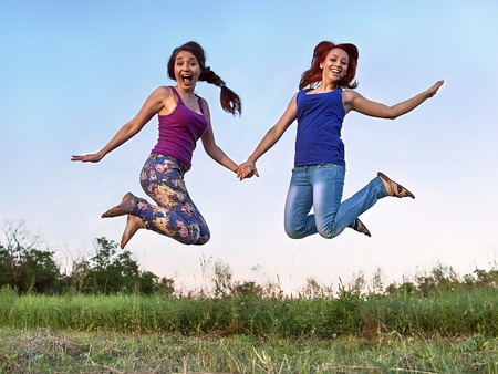 Two girls jumping in the air holding handsの写真素材